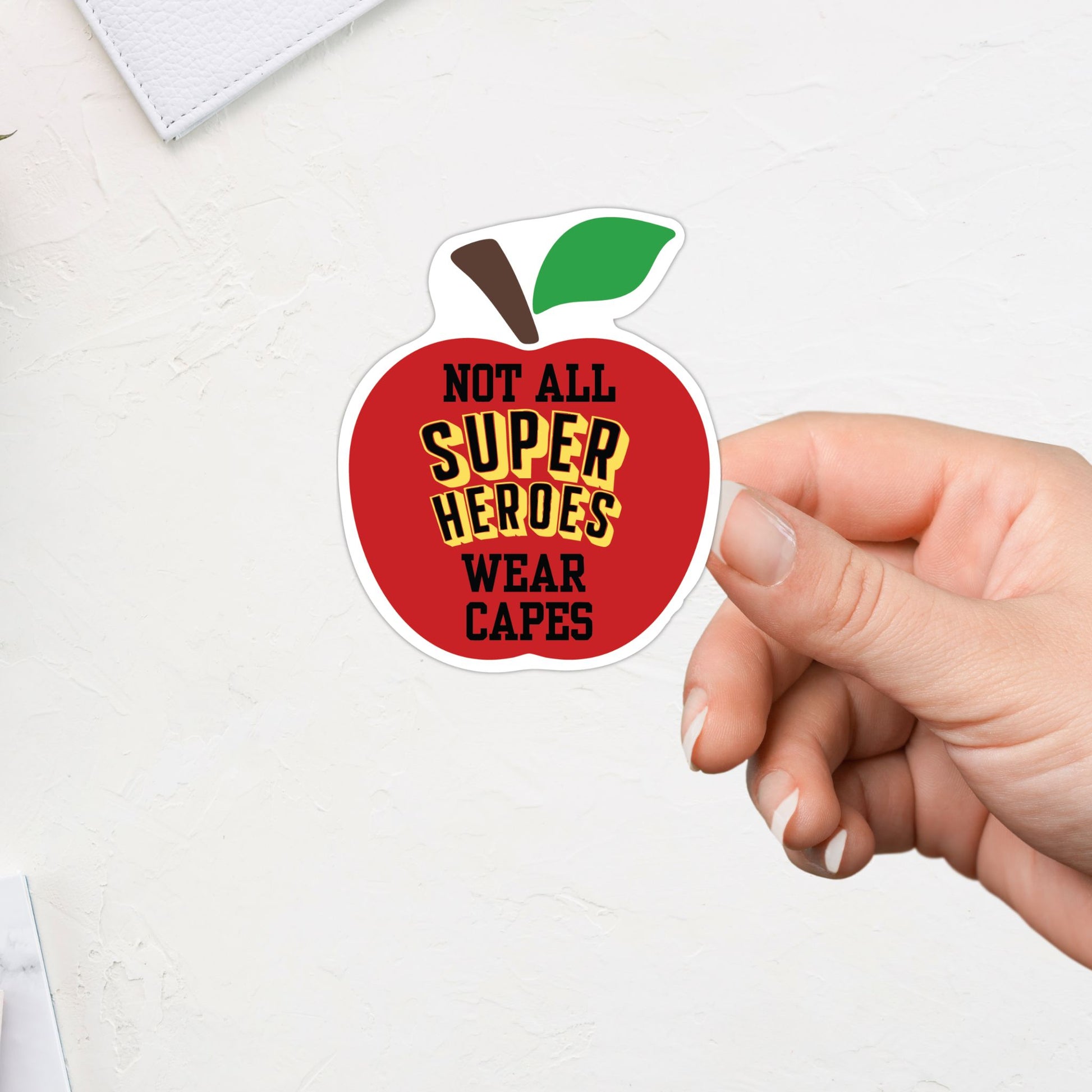 Hand holding a red apple-shaped sticker with text on a white background